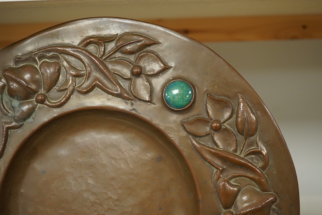 An Arts and Crafts embossed copper dish, in the manner of John Pearson, inlaid with Ruskin cabochons, unsigned, 32cm in diameter